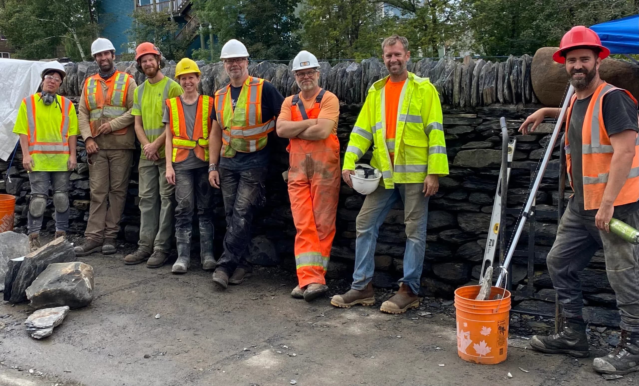 Nine members of the crew in hi-vis and hard hats lined up along the finished wall at the end of the second season, tools and buckets at their feet.