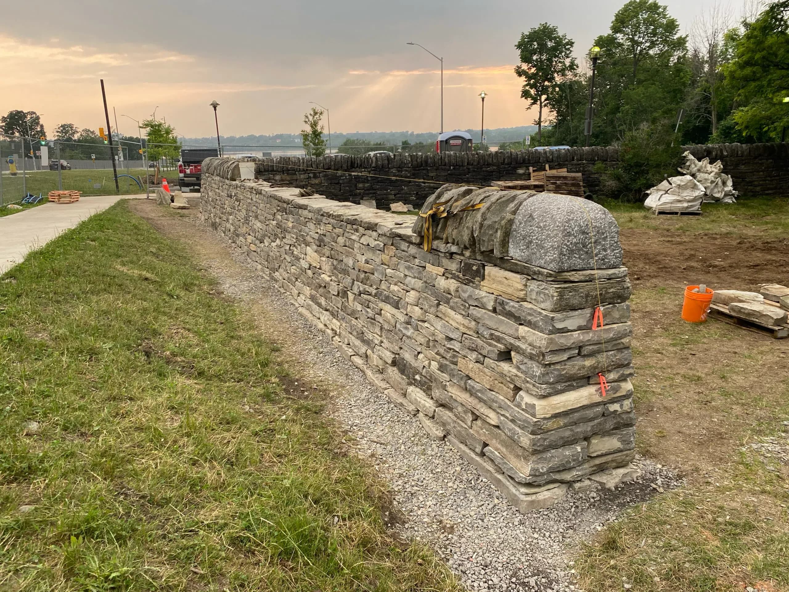 The wall built up to its coping course at sunset, the rounded bookend stone strapped in place on the end and the river behind.