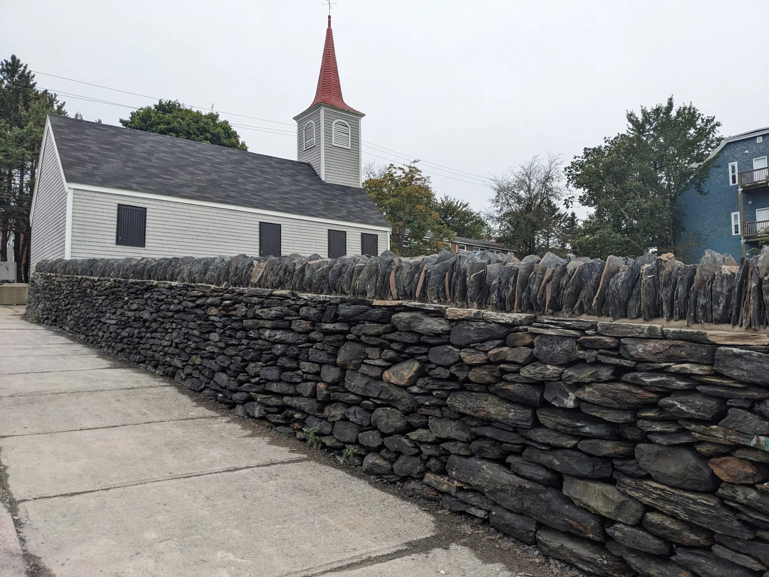 The rebuilt dry stone wall running along the sidewalk beside the white clapboard Little Dutch Church and its red steeple.