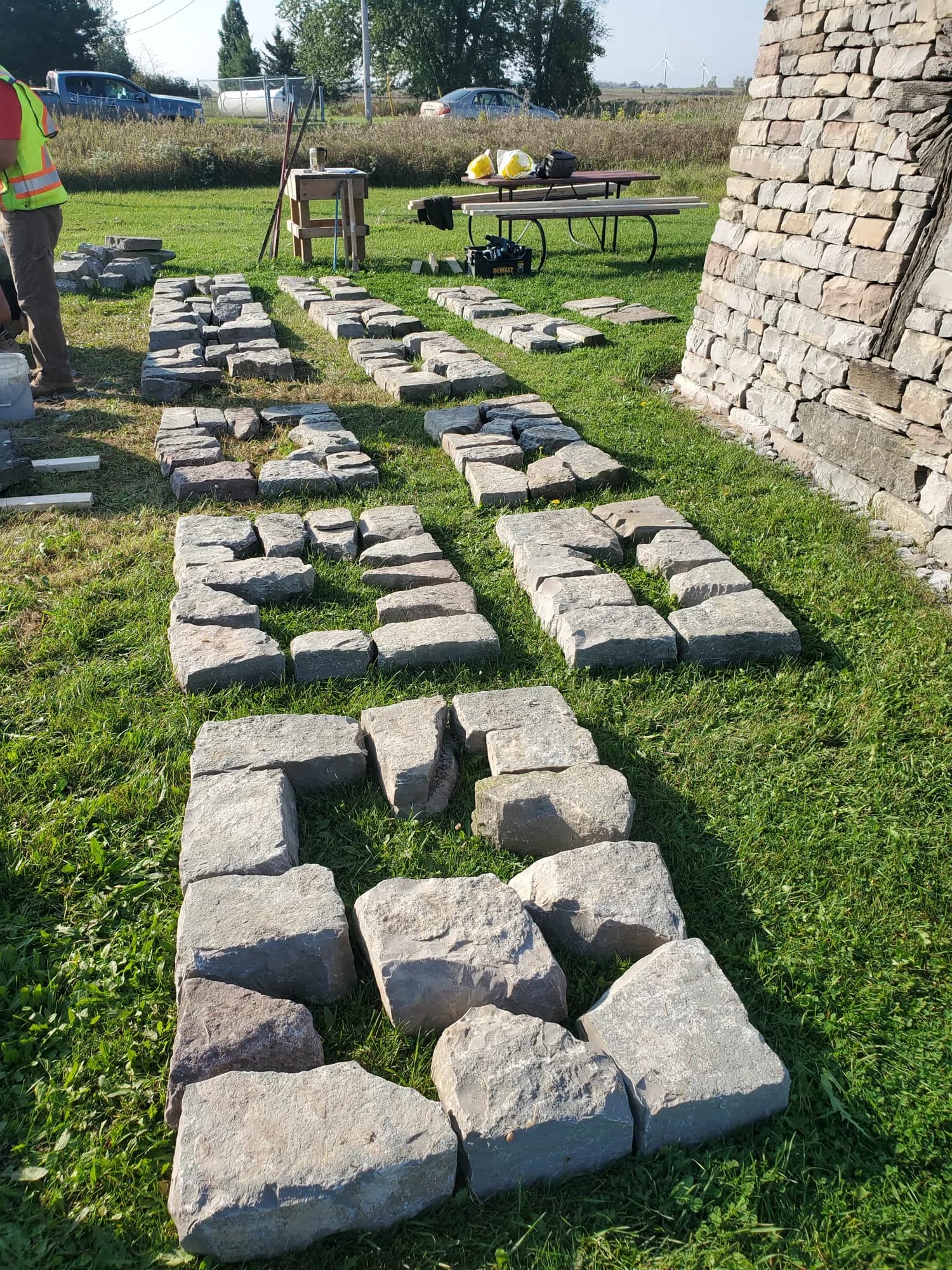 Stone from the dismantled pillar laid out in rows on the grass, kept in order, with the coursed face of one of the standing pillars at the right of the frame.