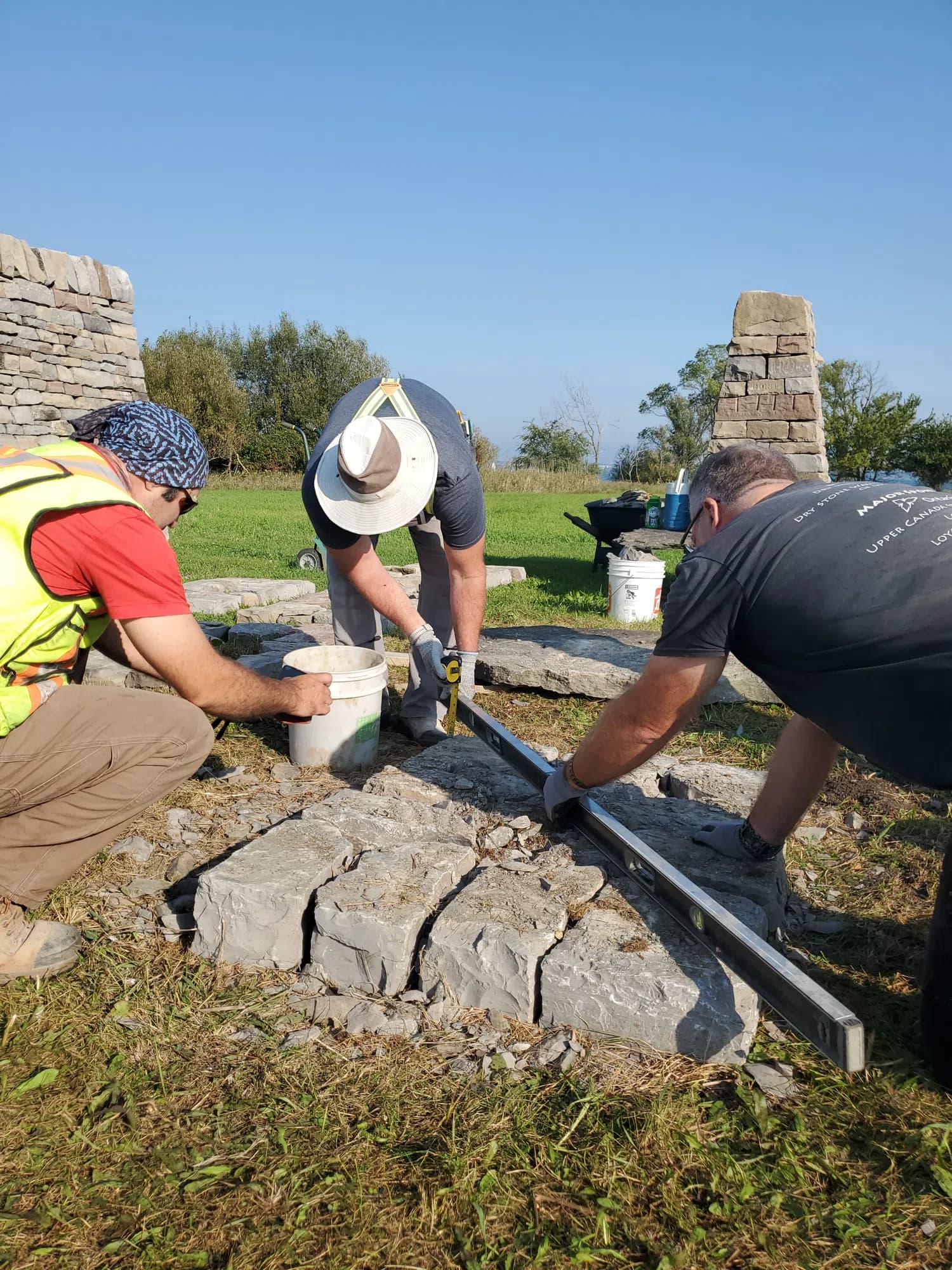Three of the crew crouched at the pillar footprint, running a long steel straightedge across the newly set foundation stones.